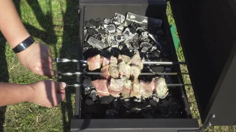 Man with smart watch flips the meat on the brazier. Pieces of meat on skewers. Stock Footage 137208634
