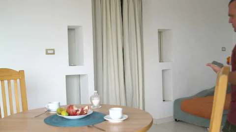 A man with a smartphone and persimmon comes to the table and sits on a chair Stock Footage 100724701