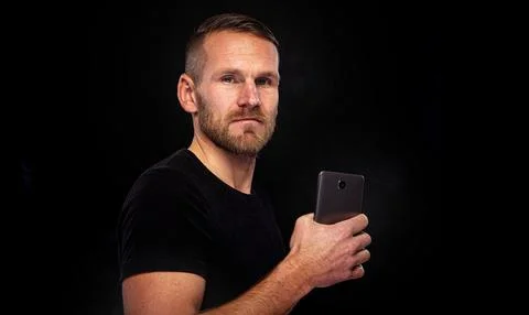 A man with a smartphone on a dark background. Stock Photos