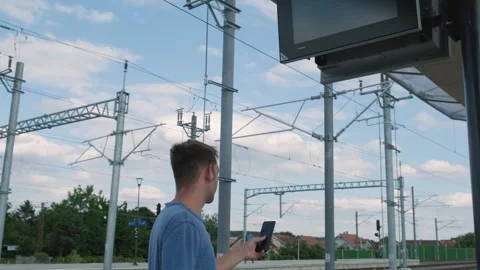 Man with smartphone looking at the train schedule at railway station. Male Stock Footage 256658130