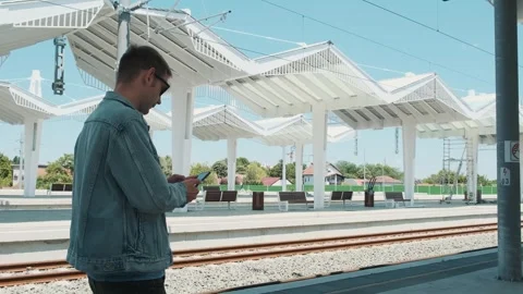 Man with smartphone looking at the train schedule at railway station. Male Stock Footage 274132789