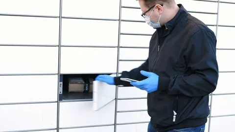 Man with smartphone in protective mask and gloves opening parcel locker Stock Footage 128879448
