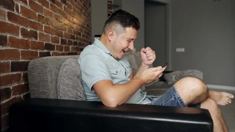 A man with a smartphone sits on a sofa. He is very happy about something Stock Footage 132647777