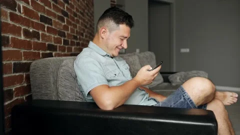 A man with a smartphone sits on a sofa. He is happy about something Video stock 132648107