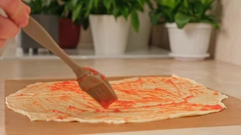 A man smears a layer of yeast dough with tomato sauce with a silicone brush Stock Footage 244803565