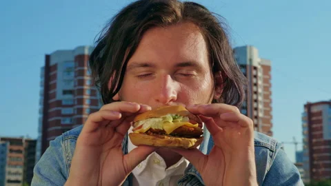A man is smelling and biting a cheeseburger with great appetite Video stock 151740606