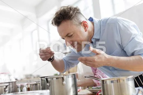 Man smelling food leaning over pot in cooking class kitchen Stock Photos