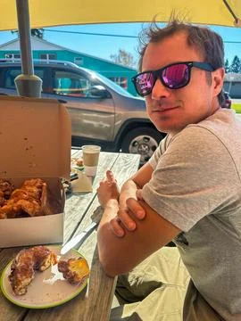 A man smiles as he eats doughnuts on a bench outside Stock Photos