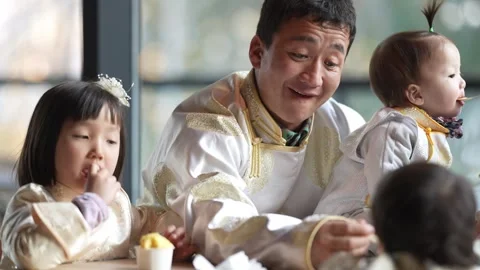 Man smiles while feeding two children at table Vidéo 338004266