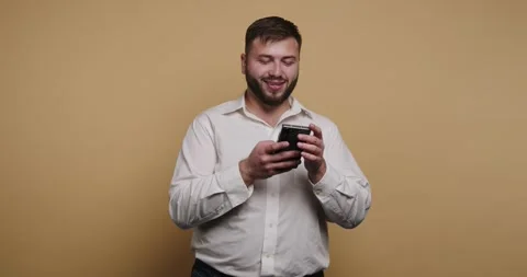 Man smiles while looking at his phone in a studio with a yellow background 스톡 동영상 326797562