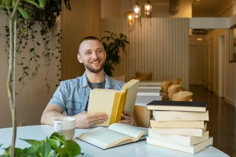 Man smiles while reading a book at a modern cafe during an online education.. Stock Photos