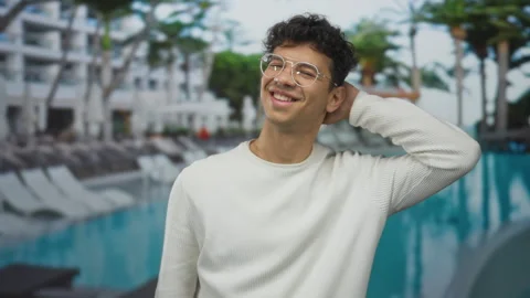 Man smiles while tilting head at resort pool adjacent to hotel building wit.. Vídeos de archivo 314643639