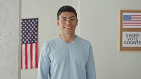 Man smiling with american flag and voting poster in a polling building; civ.. Stock Footage 339252812