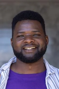Man smiling and facing camera, wearing purple crewneck with open striped shirt Stock Photos