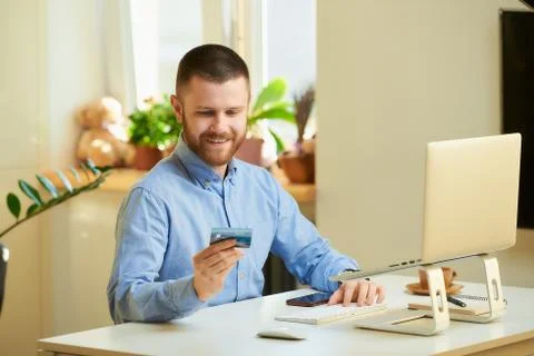 A man smiling and looking at his credit card in front of the laptop at home. Stock Photos