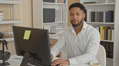 Man smiling and typing at computer with hands on keyboard amid bookshelves,.. Stock Footage 337439911