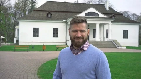 Man smiling at camera in front of big house, around dolly steadycam shot Vidéo 74345101