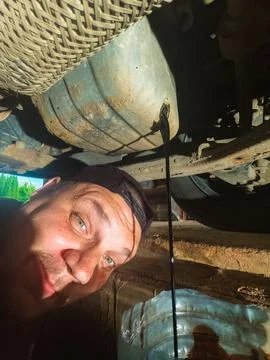 Man smiling at the camera while draining dark used engine oil from a car engines 스톡 사진