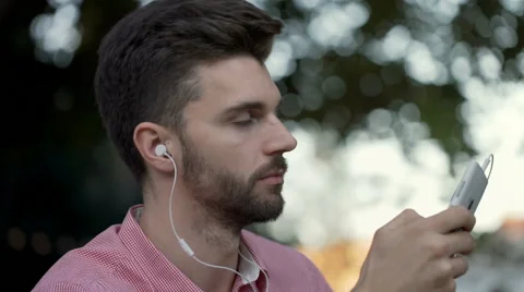 Man smiling to the camera while listening music and texting on smartphone Stock Footage
