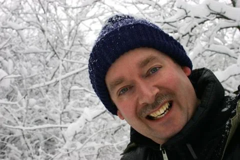 Man smiling to the camera while surrounded by snow filled branches Stock Photos