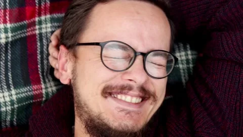 Man smiling in glasses lying on plaid blanket close up. Cozy portrait of ha.. 스톡 동영상 337346783