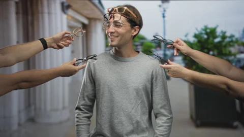 Man smiling with sunglasses on forehead as multiple hands offer eyeglasses .. Stock Footage 337436491