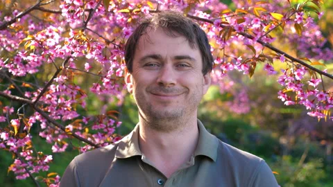 Man smiling under blooming cherry blossoms in lush, vibrant garden, Stock Footage 280020406