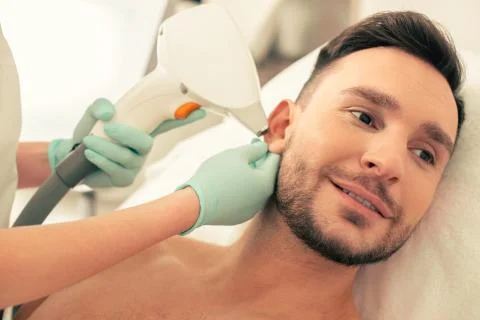 Man smiling while cosmetologist touching his ear Stock Photos
