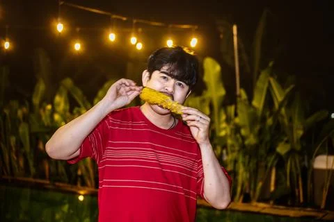 Man Smiling While Eating Roasted Corn. Man Relishing Roasted Corn Outdoors .. Stock Photos