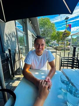 A man smiling while holding a woman's hand at a outdoor table Stock Photos