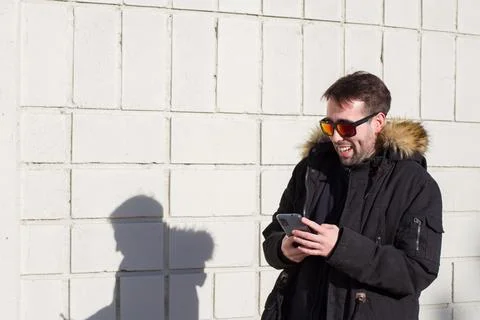 Man smiling while looking at his cell phone, wearing sunglasses and a parka Stock Photos