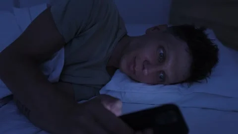Man smiling while scrolling smartphone in bed at night, enjoying social media Stockbeeldmateriaal 346247782