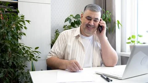 Man Smiling While Talking on Phone at Desk Fotos de archivo