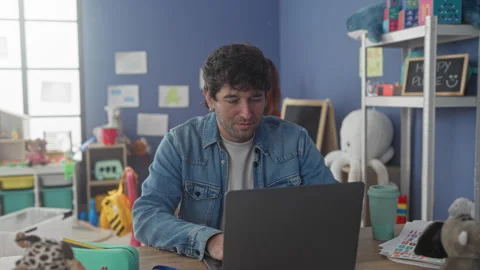 Man smiling while typing on laptop in preschool classroom with woman teache.. Stock Footage 337392761