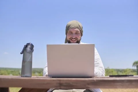 Man smiling while using a laptop outdoors, working remotely while traveling Stock Photos