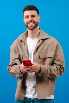 Man smiling while using a red smartphone against a bright blue background Foto stock