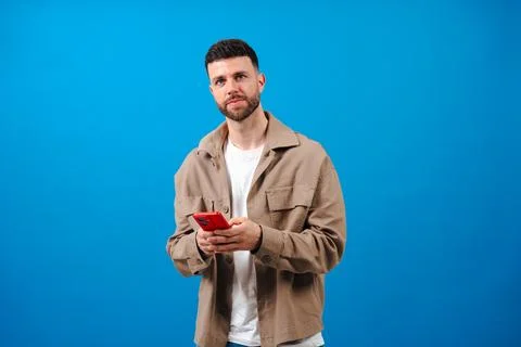 Man smiling while using a red smartphone against a bright blue background Stock-Fotos