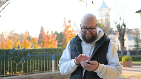 Man smiling while using smartphone in park adorned with vibrant autumn colors Stock Footage 346709532