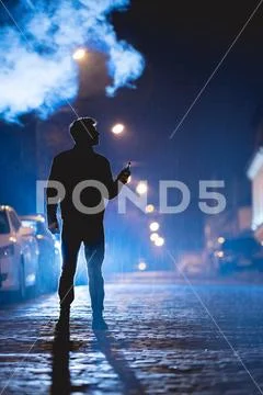 The man smoke electrical cigarette on the street. Evening night time Stock Photos
