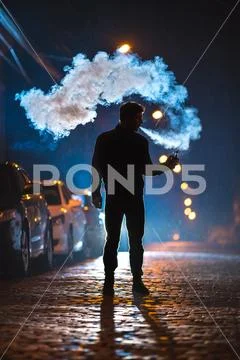 The man smoke electrical cigarette in the street. Evening night time Stock Photos