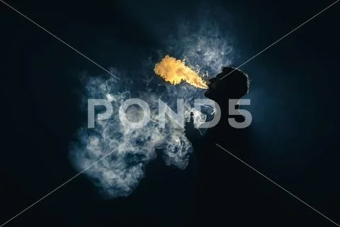 The man smoke an electronic cigarette against the background of bright light Stock Photos