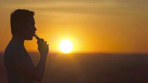 The man smoke electronic cigarette on the background of a sunset Video stock 76900681