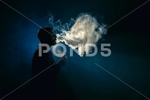 The man smoke an electronic cigarette on the background of the bright light Stock Photos