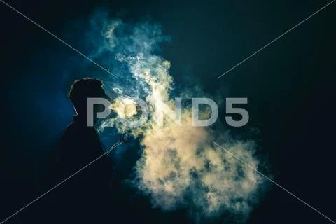 The man smoke an electronic cigarette on the dark background Stock Photos