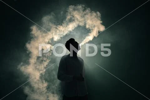 The man smoke an electronic cigarette on the dark background Stock Photos