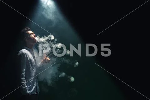 The man smoke an electronic cigarette with a ring and on the dark background Stock Photos