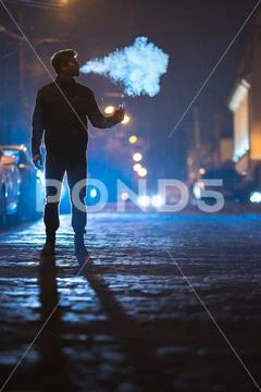 The man smoke electronic cigarette on the street. Evening night time Stock Photos