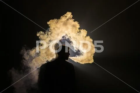 The man smoke an electronic cigarette on the yellow light background Stock Photos