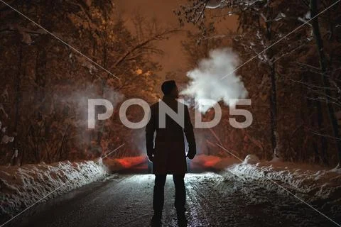 The man smoke on the snowy road in the forest. evening night time Stock Photos