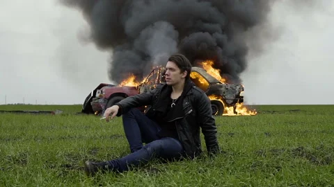 Man smokes against the background of a burning car, despair, a fire, an Stock Footage 95201078